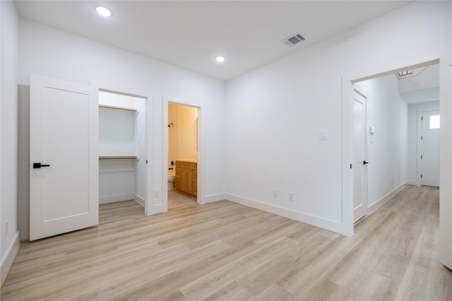 unfurnished bedroom with a closet, ensuite bath, a walk in closet, and light hardwood / wood-style flooring