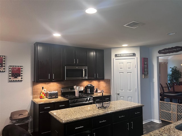 kitchen with light stone countertops, backsplash, a center island, and stainless steel appliances