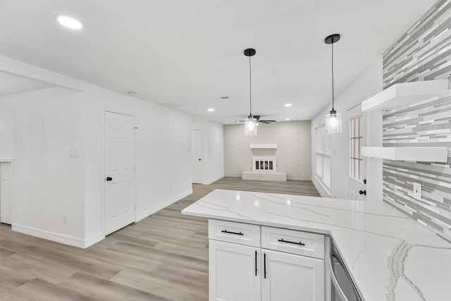 kitchen featuring decorative backsplash, light stone countertops, pendant lighting, a fireplace, and white cabinetry