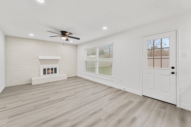 unfurnished living room featuring light hardwood / wood-style flooring, a brick fireplace, ceiling fan, and brick wall