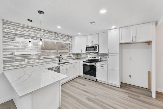 kitchen featuring appliances with stainless steel finishes, decorative light fixtures, white cabinetry, and light stone counters