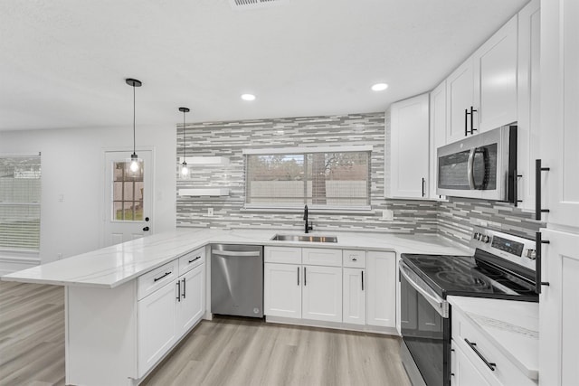 kitchen with sink, stainless steel appliances, kitchen peninsula, decorative light fixtures, and white cabinets