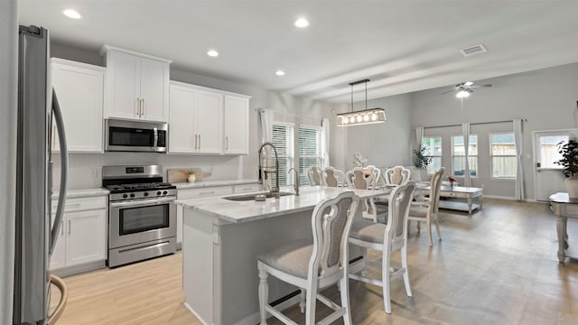 kitchen featuring appliances with stainless steel finishes, decorative light fixtures, white cabinetry, and an island with sink