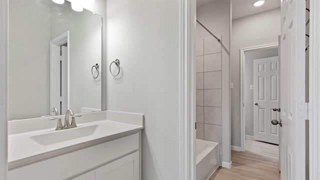 bathroom with hardwood / wood-style flooring, tiled shower / bath combo, and vanity