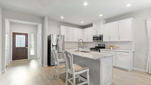 kitchen featuring sink, white cabinets, stainless steel appliances, and a center island with sink