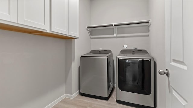 laundry room featuring cabinets, washing machine and dryer, and light hardwood / wood-style flooring