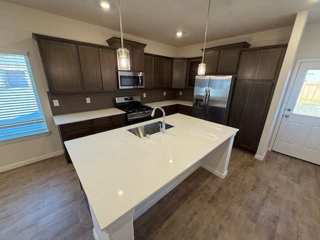 kitchen with appliances with stainless steel finishes, a kitchen island with sink, sink, hardwood / wood-style floors, and hanging light fixtures