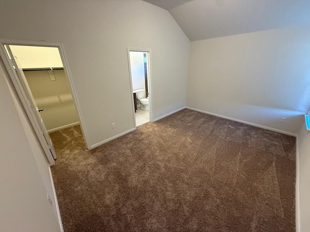 unfurnished bedroom with dark colored carpet, vaulted ceiling, a walk in closet, and a closet