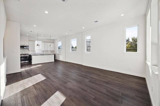 unfurnished living room featuring sink, a healthy amount of sunlight, and dark hardwood / wood-style floors