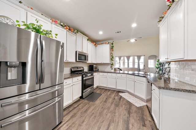 kitchen featuring appliances with stainless steel finishes, white cabinetry, sink, dark stone counters, and kitchen peninsula