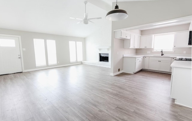 kitchen with light hardwood / wood-style floors, ceiling fan, a fireplace, white cabinets, and sink