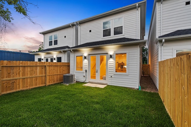 back house at dusk with a lawn, french doors, and cooling unit