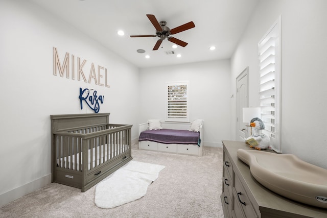 carpeted bedroom featuring a nursery area and ceiling fan