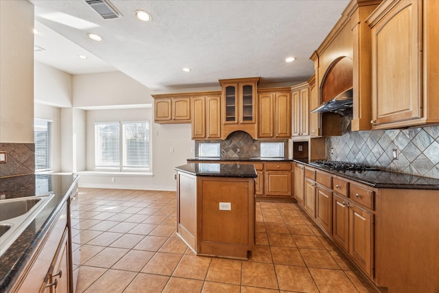 kitchen with dark stone countertops, tasteful backsplash, a center island, and light tile patterned flooring