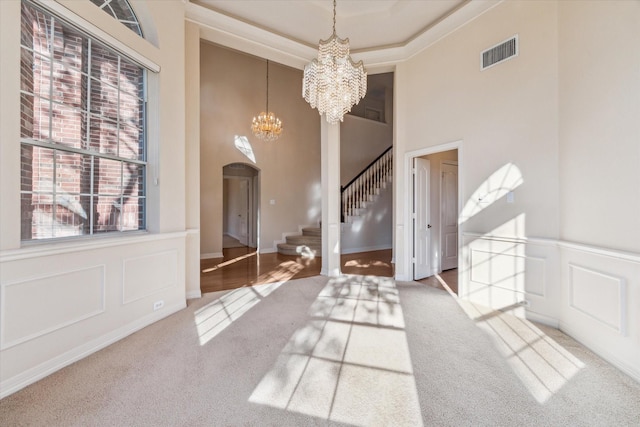 entryway with an inviting chandelier, a towering ceiling, a raised ceiling, and carpet