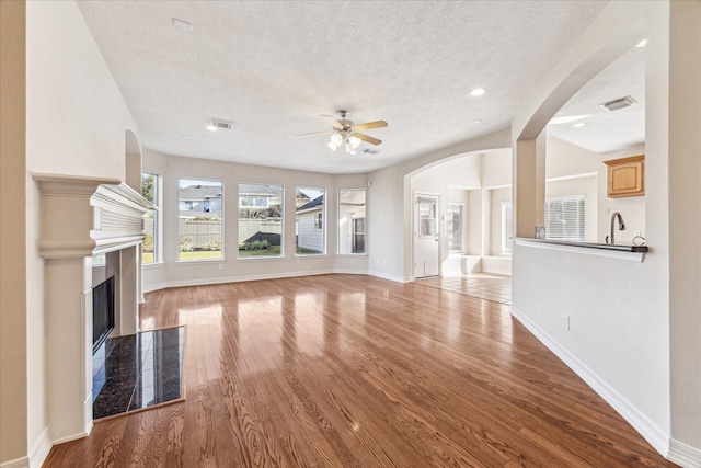 unfurnished living room with sink, a textured ceiling, ceiling fan, and light hardwood / wood-style floors