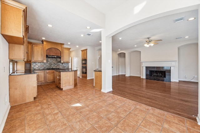 kitchen with tasteful backsplash, light tile patterned floors, a kitchen island, ceiling fan, and a fireplace