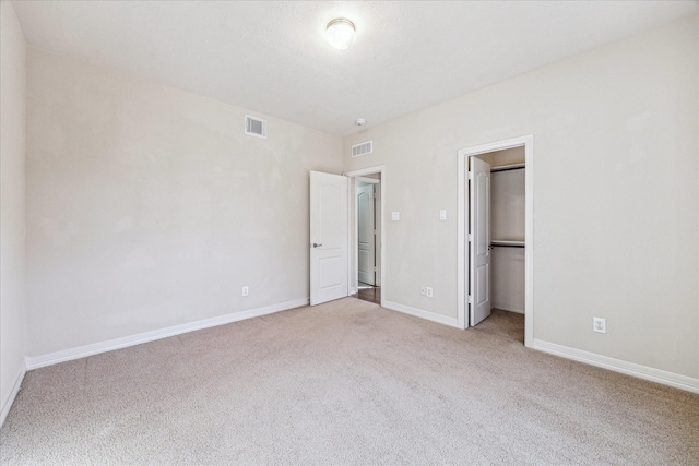 unfurnished bedroom with a walk in closet, light colored carpet, and a closet