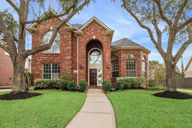 traditional-style house featuring a front yard, fence, a shingled roof, and brick siding