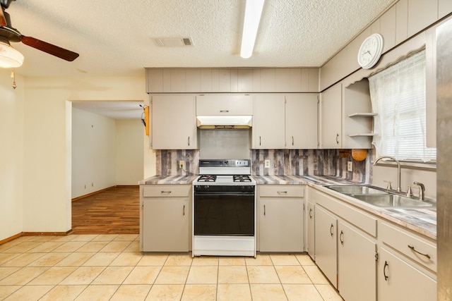 kitchen with light tile patterned floors, decorative backsplash, gas stove, a textured ceiling, and sink