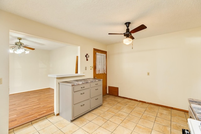 kitchen featuring ceiling fan, kitchen peninsula, light tile patterned flooring, and a textured ceiling