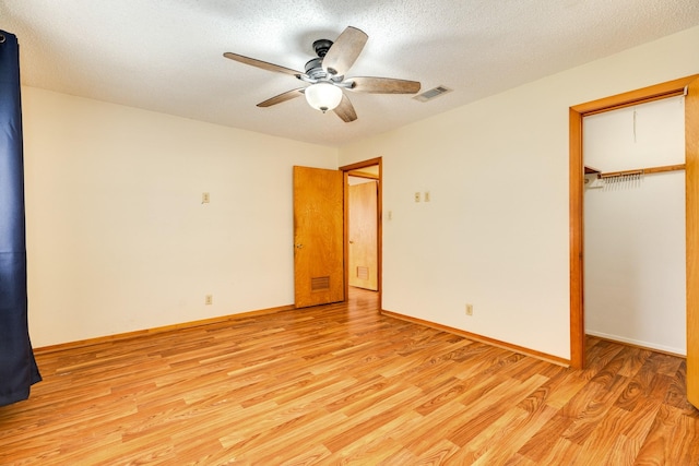 unfurnished bedroom with a spacious closet, ceiling fan, a closet, a textured ceiling, and light hardwood / wood-style flooring