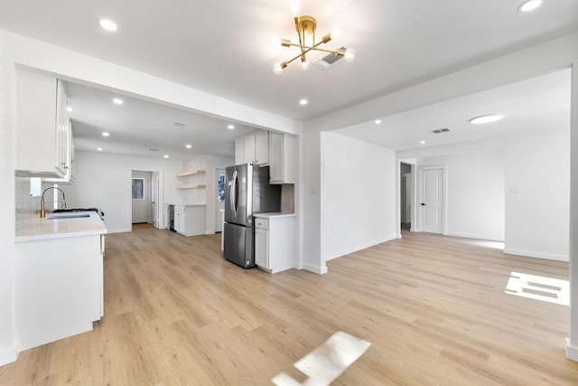 kitchen featuring white cabinets, sink, stainless steel refrigerator, and an inviting chandelier