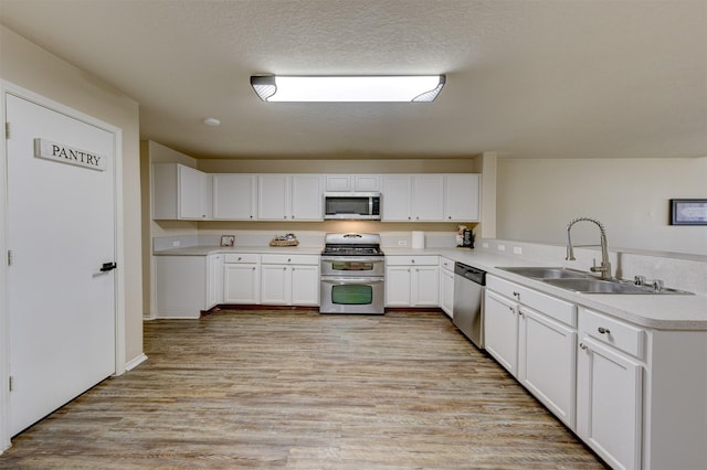 kitchen featuring appliances with stainless steel finishes, light wood-type flooring, a textured ceiling, sink, and white cabinets