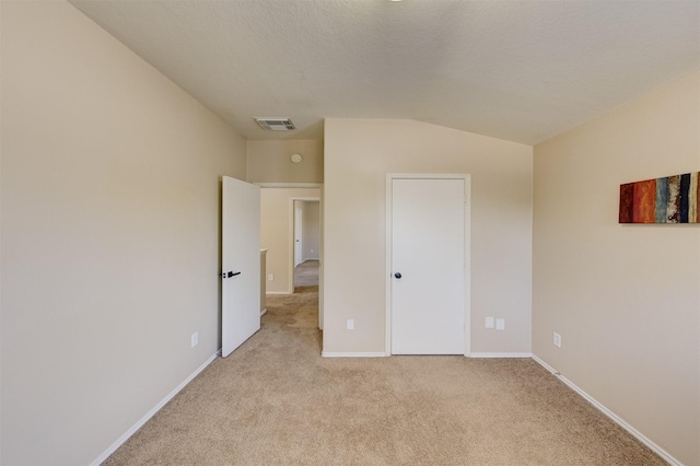 unfurnished bedroom with a textured ceiling, light colored carpet, and vaulted ceiling