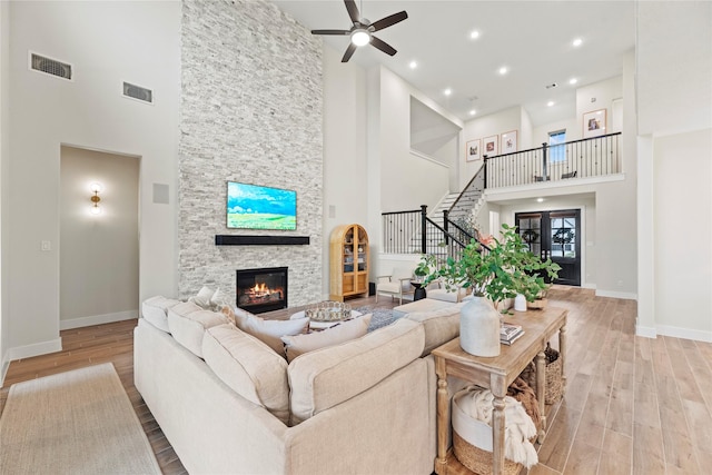 living room featuring a towering ceiling, light hardwood / wood-style flooring, a stone fireplace, and ceiling fan