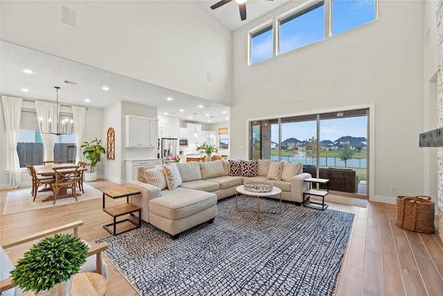 living room with a healthy amount of sunlight, a water view, a towering ceiling, and light hardwood / wood-style flooring