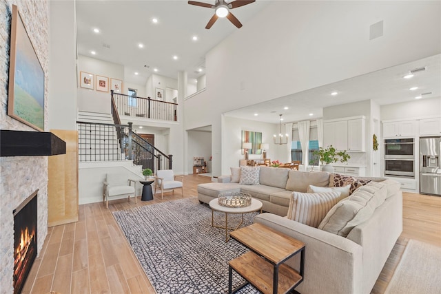 living room featuring a stone fireplace, ceiling fan, light hardwood / wood-style floors, and a high ceiling