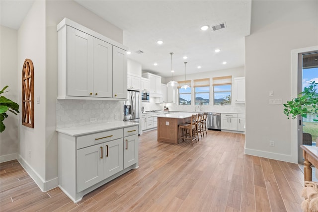 kitchen featuring pendant lighting, a center island, appliances with stainless steel finishes, white cabinetry, and a breakfast bar area