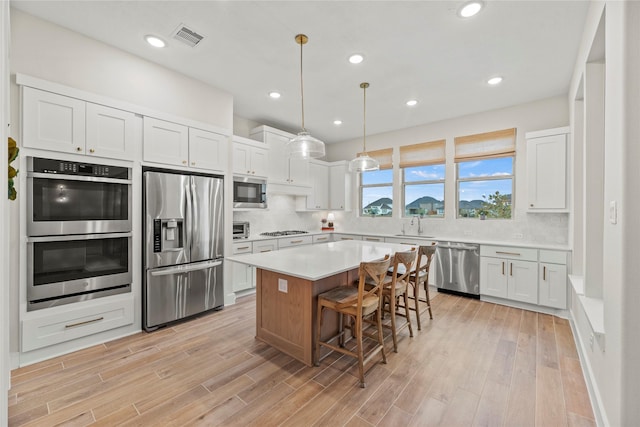 kitchen with white cabinetry, a center island, stainless steel appliances, decorative light fixtures, and a breakfast bar area