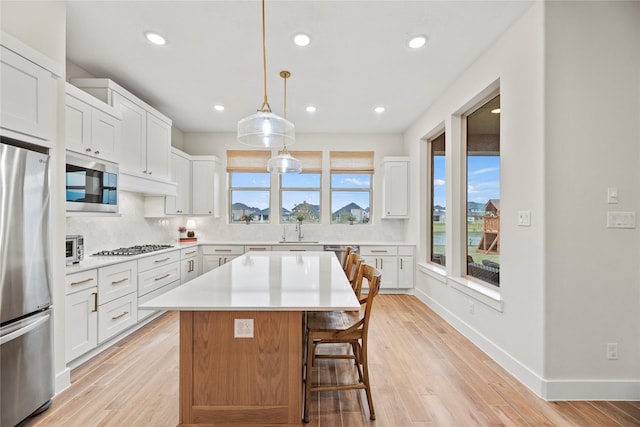 kitchen with white cabinets, decorative light fixtures, stainless steel appliances, and a kitchen island