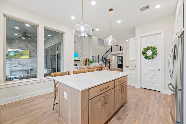 kitchen featuring pendant lighting, a breakfast bar, light brown cabinets, a kitchen island, and stainless steel refrigerator