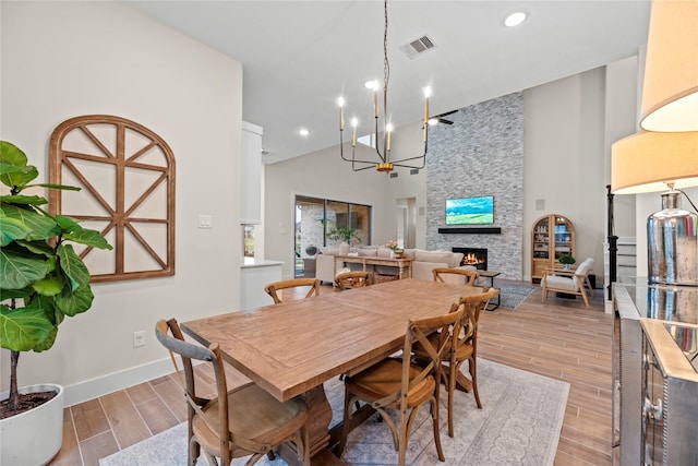 dining room featuring a stone fireplace, a chandelier, and a high ceiling