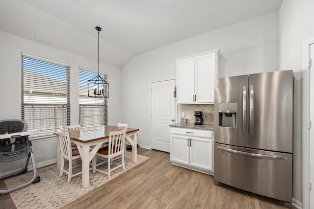 kitchen featuring white cabinetry, light stone countertops, stainless steel fridge with ice dispenser, backsplash, and vaulted ceiling