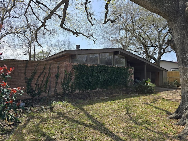 view of side of property featuring a sunroom, fence, a lawn, and brick siding