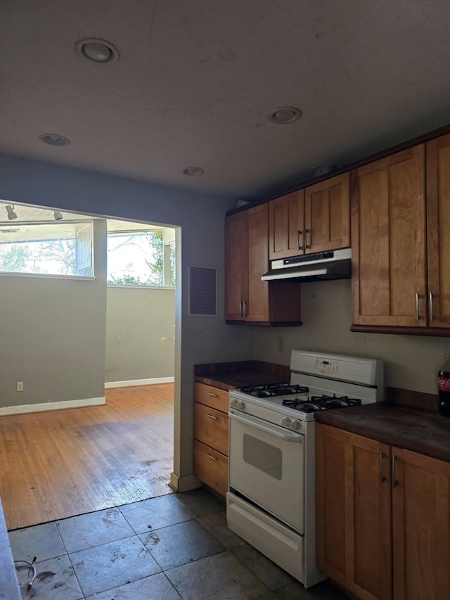 kitchen featuring gas range gas stove, dark countertops, brown cabinetry, and under cabinet range hood