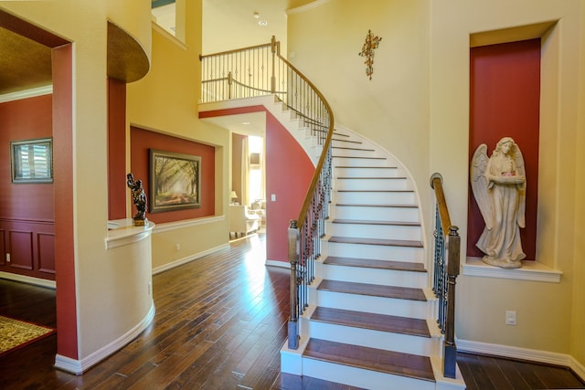 staircase featuring a high ceiling, ornamental molding, and wood-type flooring