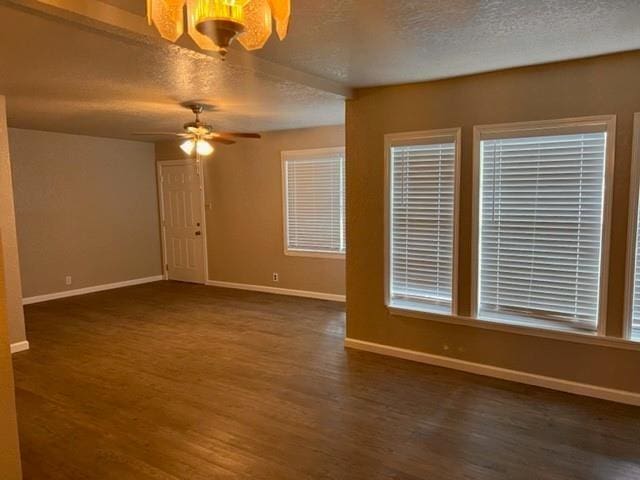 spare room featuring a textured ceiling, ceiling fan with notable chandelier, and dark wood-type flooring