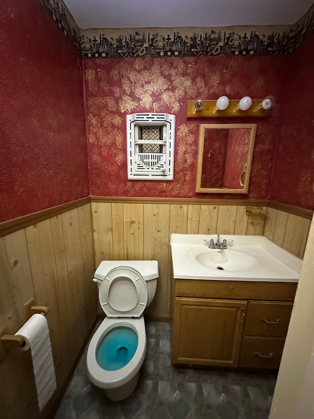 bathroom with toilet, wooden walls, and vanity