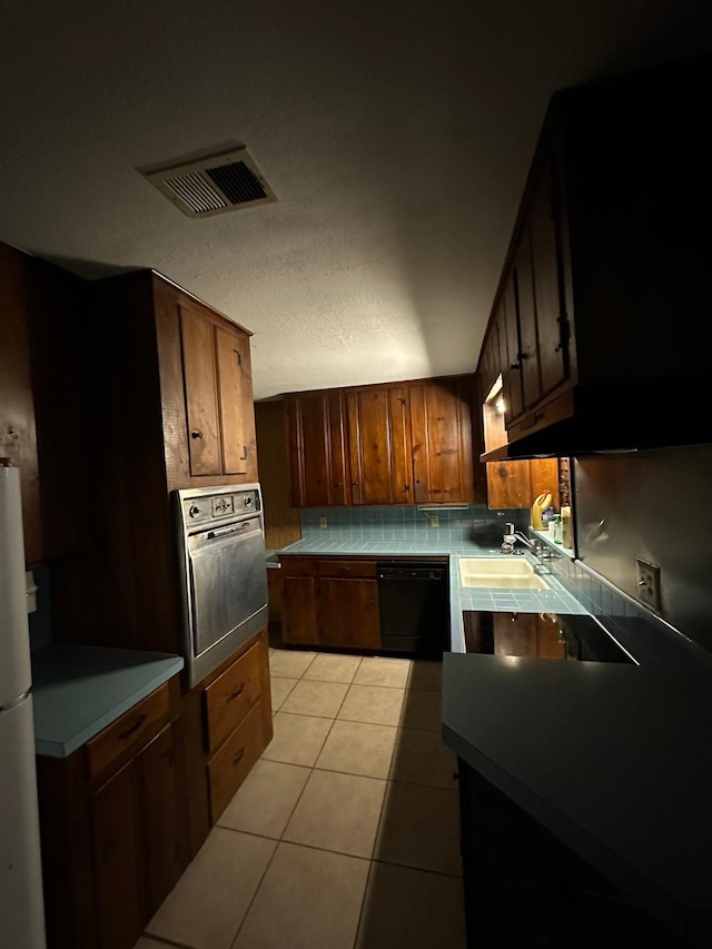 kitchen with white fridge, stainless steel oven, light tile patterned floors, sink, and black dishwasher