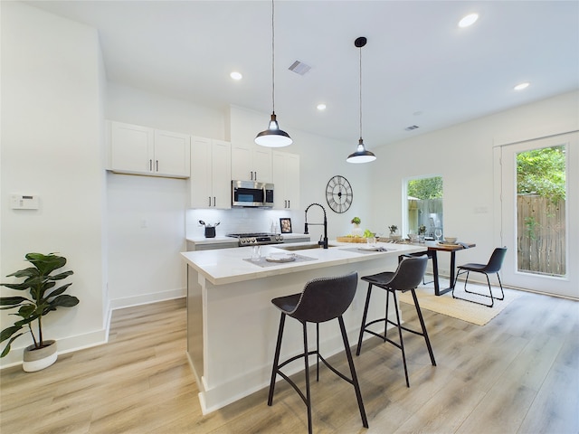 kitchen with white cabinetry, stainless steel appliances, light hardwood / wood-style floors, decorative light fixtures, and a center island with sink