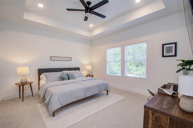 bedroom with light colored carpet, a raised ceiling, and ceiling fan