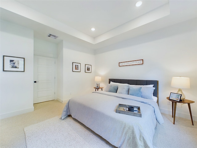 bedroom with a raised ceiling and light colored carpet