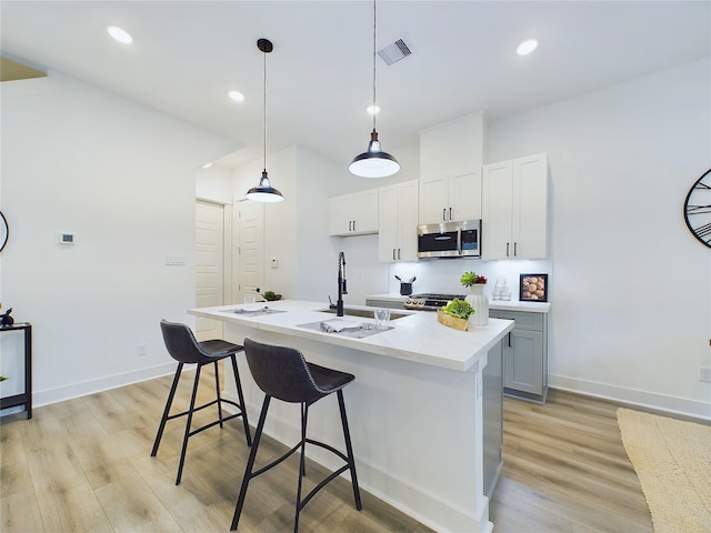 kitchen featuring stainless steel appliances, a kitchen island with sink, sink, pendant lighting, and light hardwood / wood-style floors