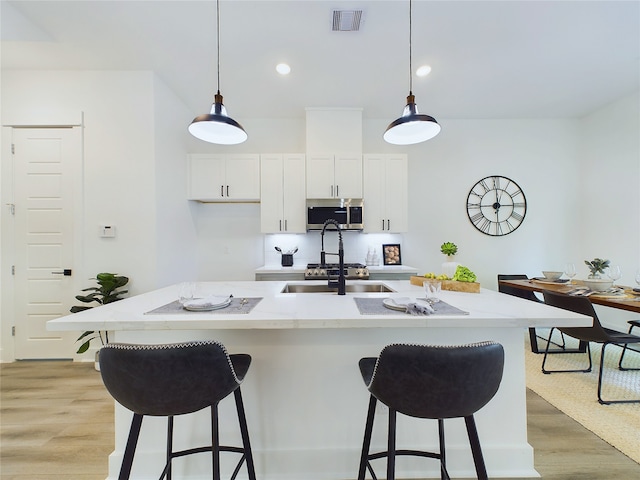 kitchen with decorative light fixtures, white cabinetry, and a kitchen island with sink