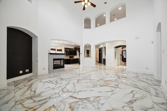 unfurnished living room with ceiling fan, a high ceiling, and a tiled fireplace